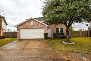 Stylish home with a brick facade, a well-manicured lawn, and a mature tree providing shade.