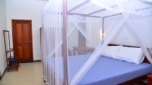 Un dormitorio con una cama cubierta por una mosquitera, una puerta de madera y una mesita.