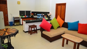 Una sala de estar moderna con un sofá, cojines coloridos, una pequeña mesa de madera y una cocina al fondo.