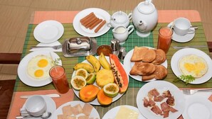 Una mesa de desayuno con diversos platos, incluyendo huevos, tostadas, plátanos y frutas tropicales.