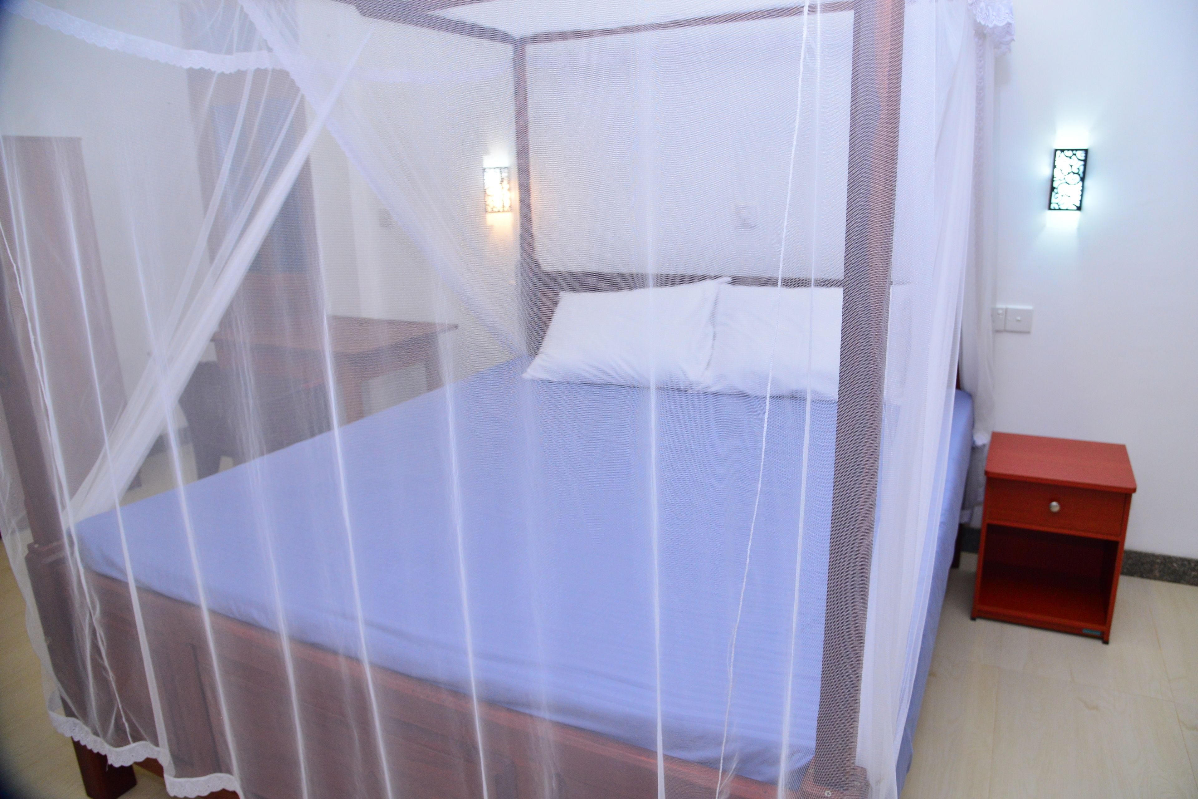 A bed with a white canopy, a red nightstand, and a wall-mounted light fixture.