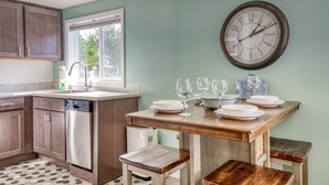Een keuken met houten kastjes, een RVS vaatwasser, een houten eettafel met banken en een wandklok.