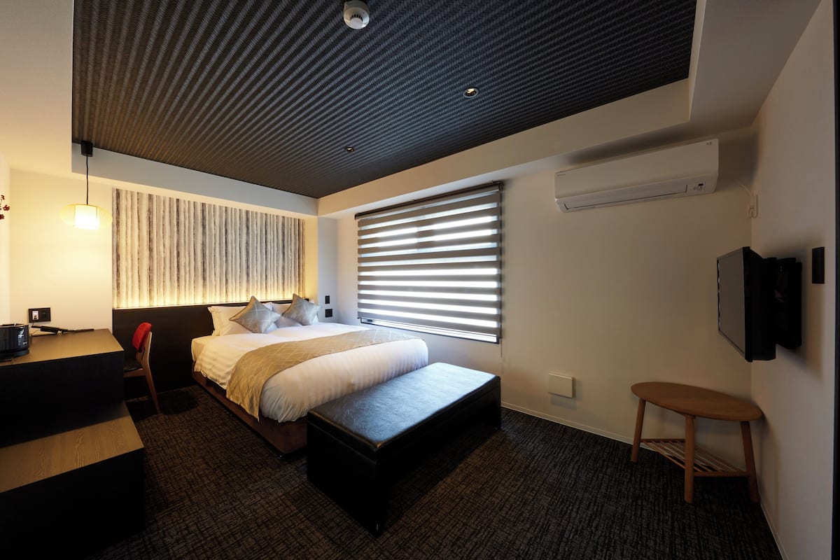 A modern hotel room with a large bed, a desk, a chair, and a TV mounted on the wall.