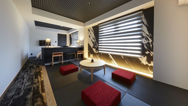Un intérieur moderne comprenant un espace cuisine, un coin salon avec des coussins rouges et une grande fenêtre équipée de stores.