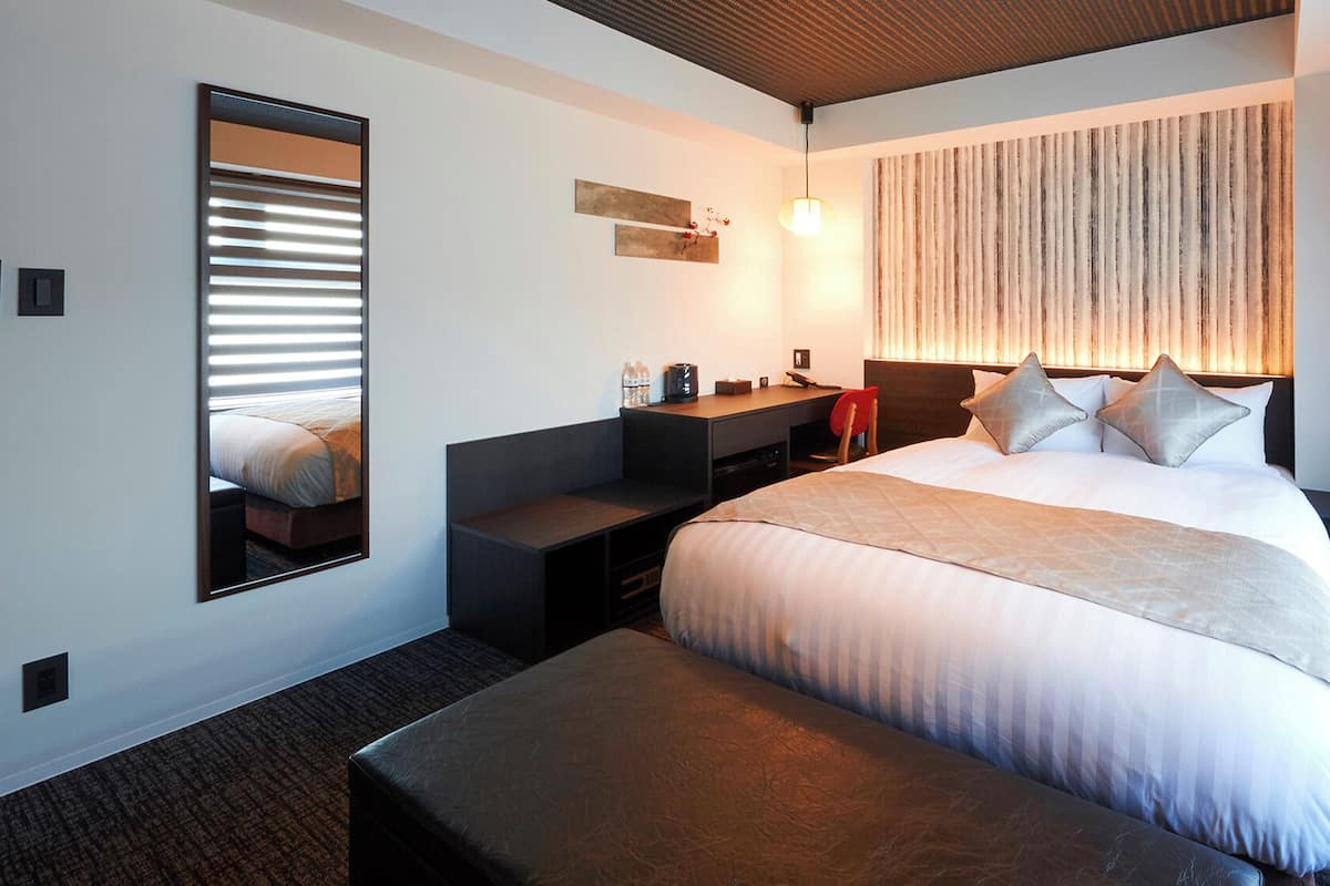 Ein Hotelzimmer mit einem Bett, einem Schreibtisch, einem Stuhl, einem Spiegel und einer Wandleuchte.
