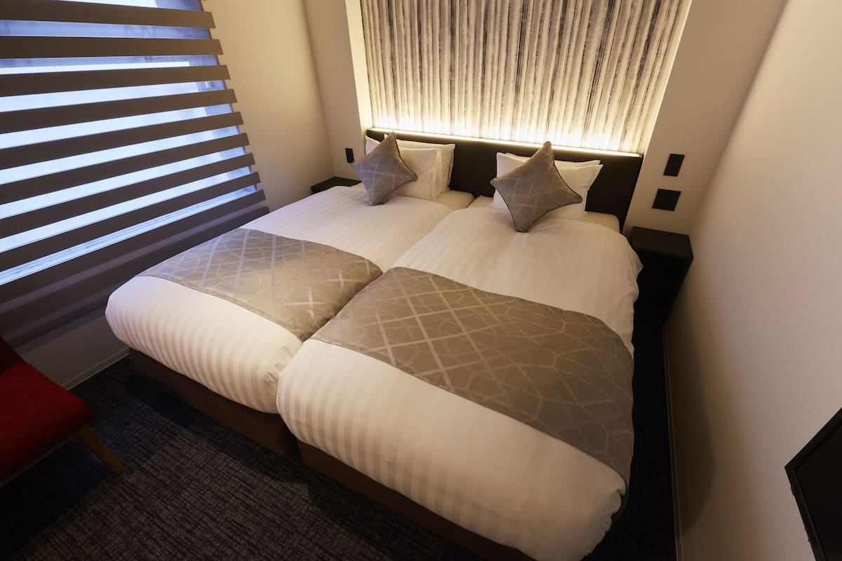A double bed with a headboard, two bedside tables, and a window with blinds.