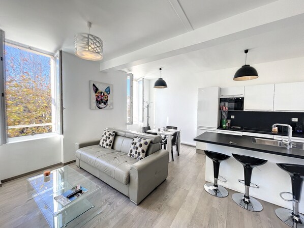 A modern kitchen with a dining area, a sofa with patterned cushions, and a glass coffee table.