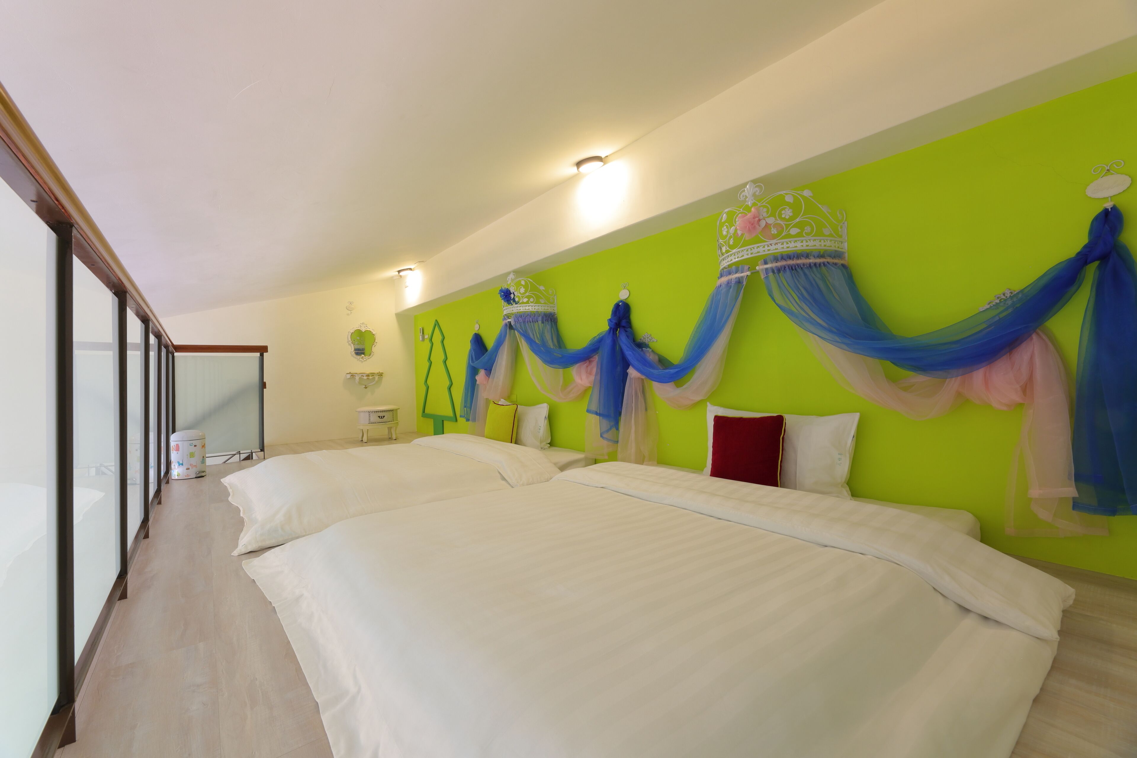 A hotel room with two beds, a green accent wall, and a canopy bed with a crown.