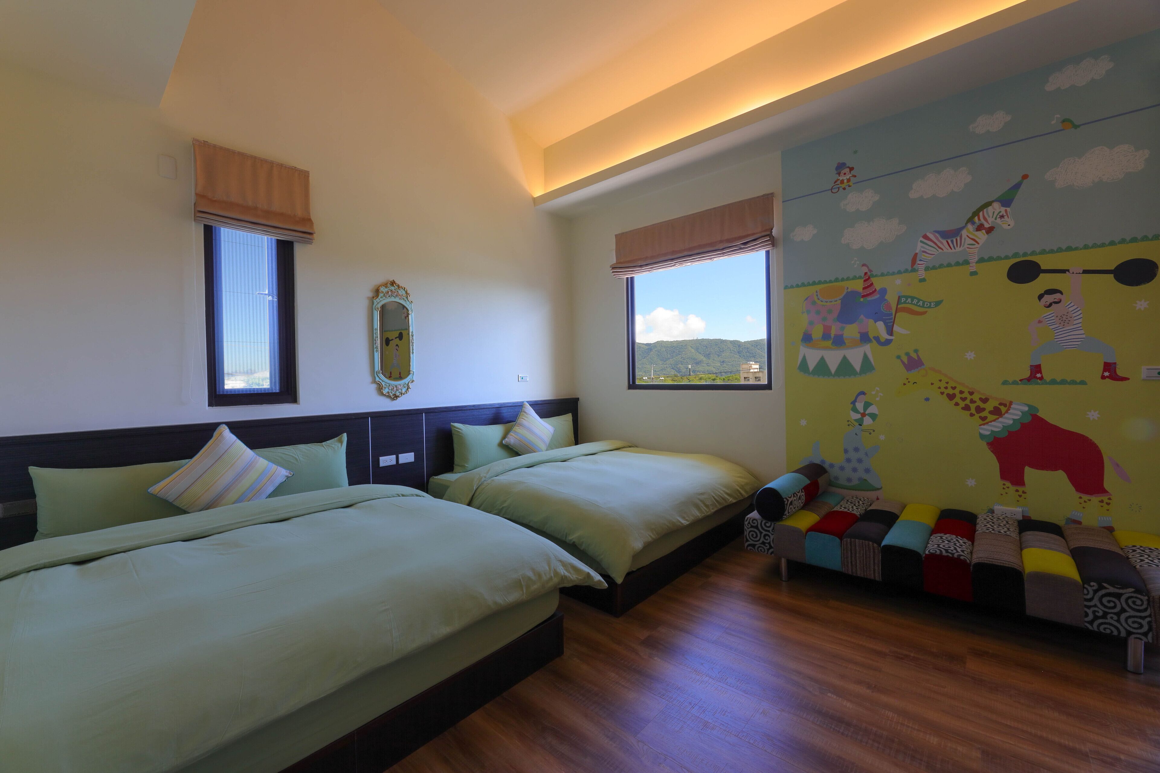 A hotel room with two beds, a large window, and a colorful mural on the wall.