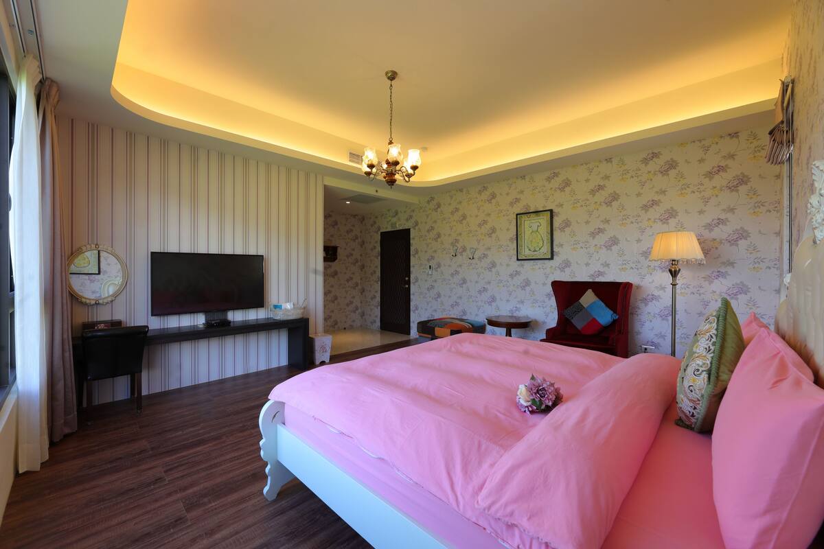 A hotel room with a large bed, a TV, a desk, and a chair.