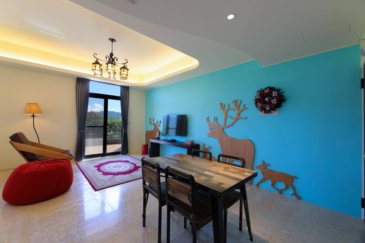 A modern living room with a wooden dining table, red bean bag, and a TV on a stand.
