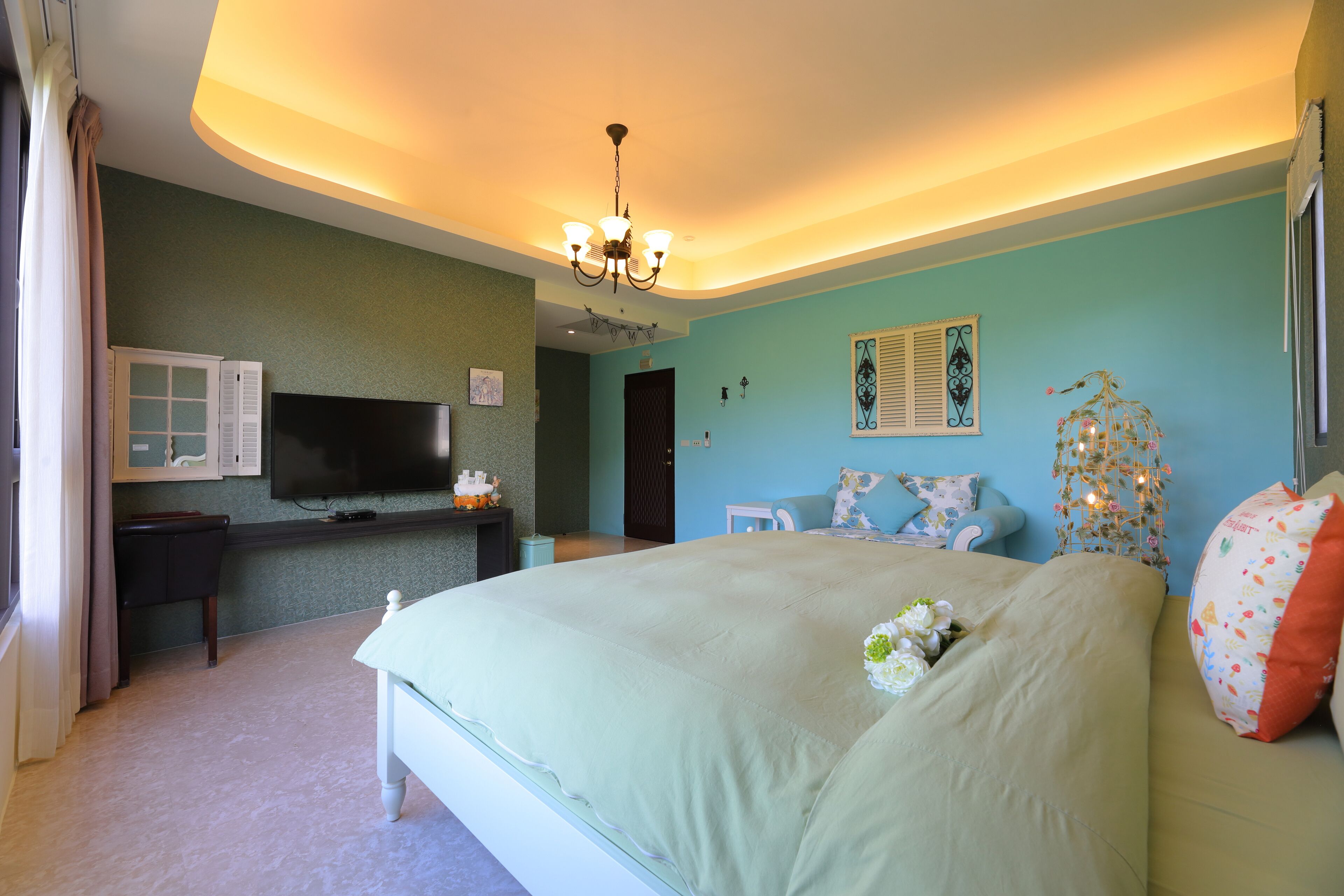 A bedroom with a large bed, a television, a desk, and a chandelier.