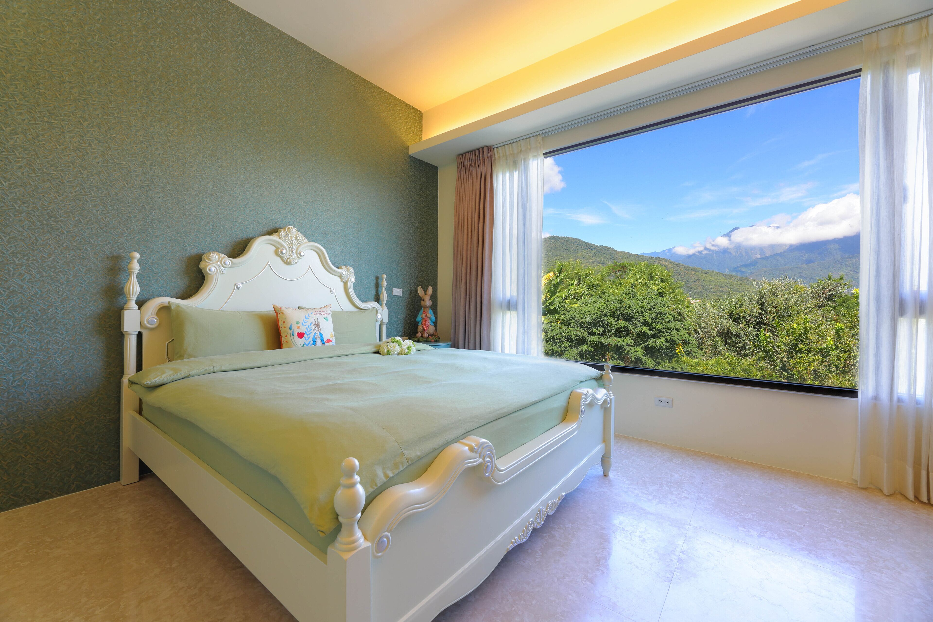 A bedroom with a large window, a bed, and a view of greenery.