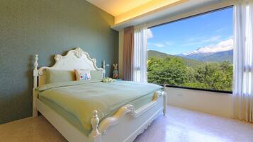 A bedroom with a large window, a bed, and a view of greenery.
