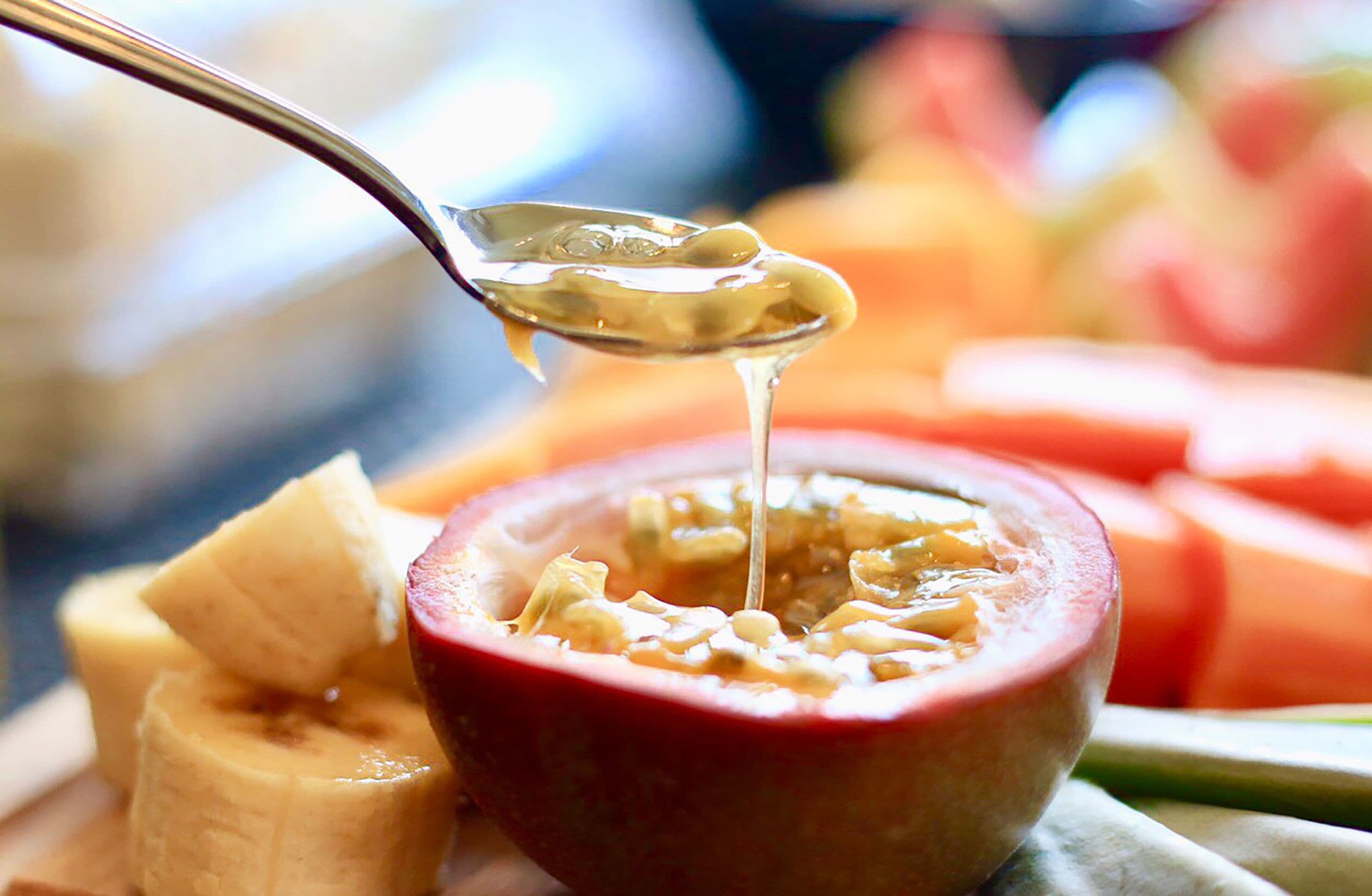A spoonful of porridge being lifted from a bowl, surrounded by sliced fruits.