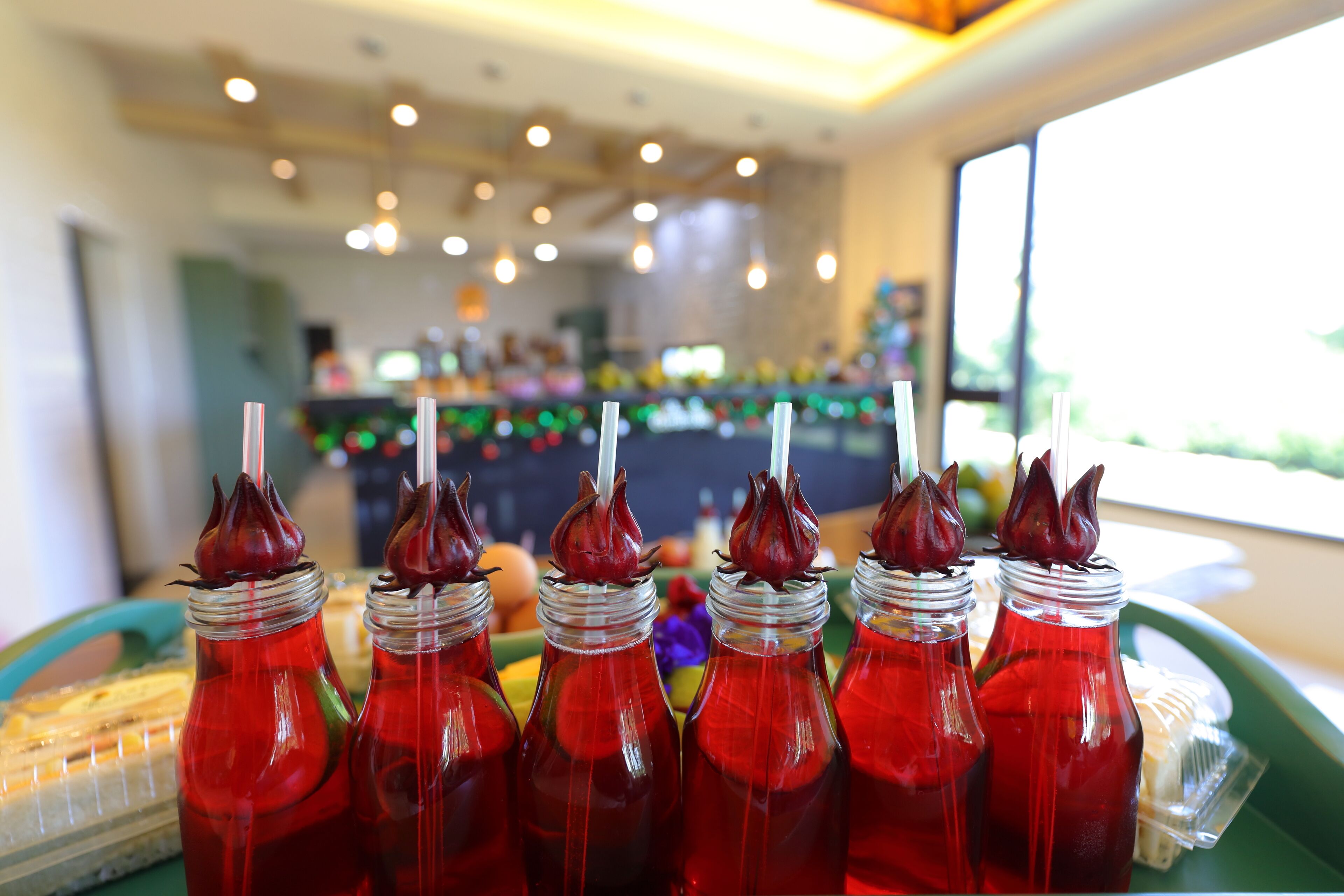 Uma fileira de garrafas vermelhas de bebidas com tampas decorativas, dispostas numa bandeja.