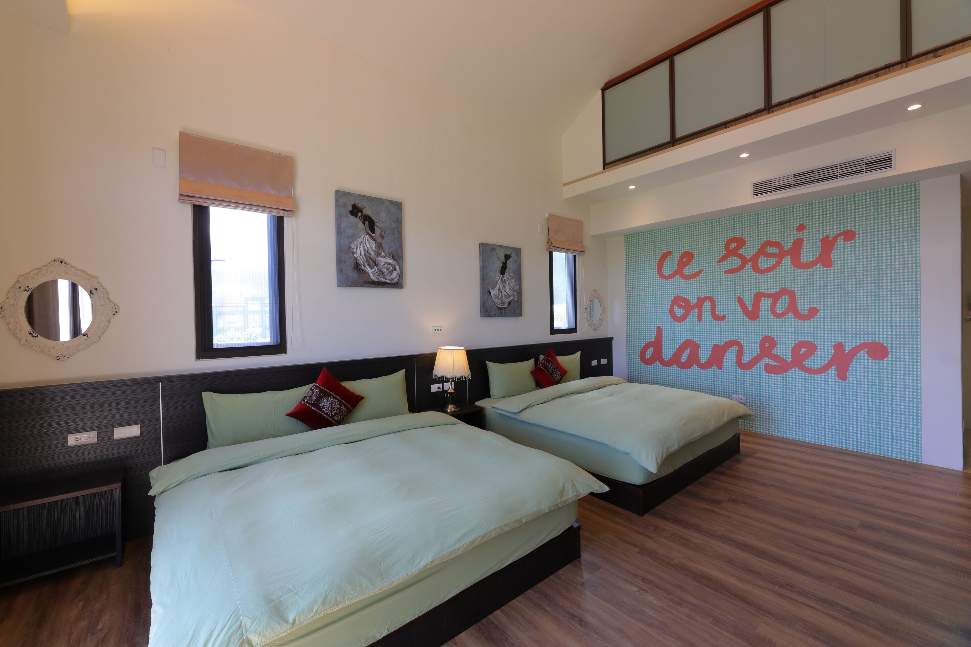 Habitación de hotel con dos camas, un ventanal grande, obras de arte en las paredes y un cartel que dice 'le soir on va danser'.