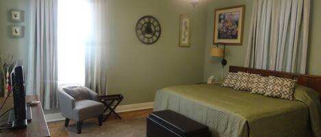A bedroom with a bed, a chair, a desk with a computer, and a clock on the wall.
