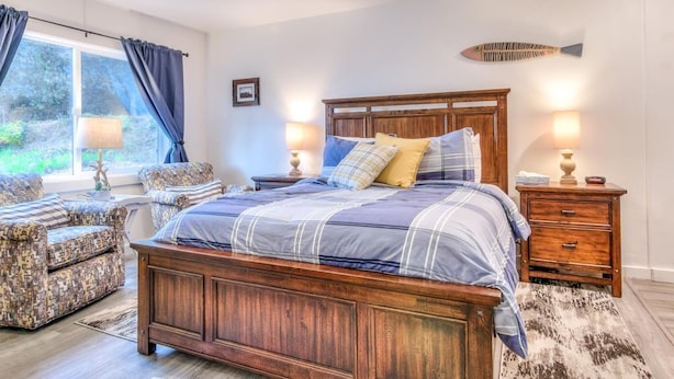 A bedroom with a large bed, a wooden nightstand, a chair, and a window with curtains.