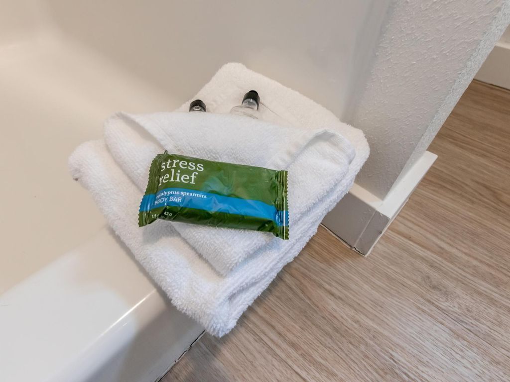 Une serviette blanche est posée sur une baignoire blanche. Sur le dessus, on aperçoit un emballage vert et bleu sur lequel est inscrit : « savon relaxant pour le corps ».