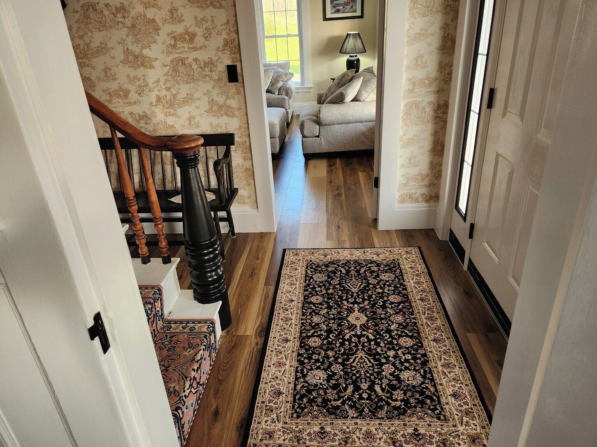 Un pasillo con una escalera de madera, una alfombra estampada y un sofá al fondo.