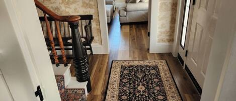 Un pasillo con una escalera de madera, una alfombra estampada y un sofá al fondo.