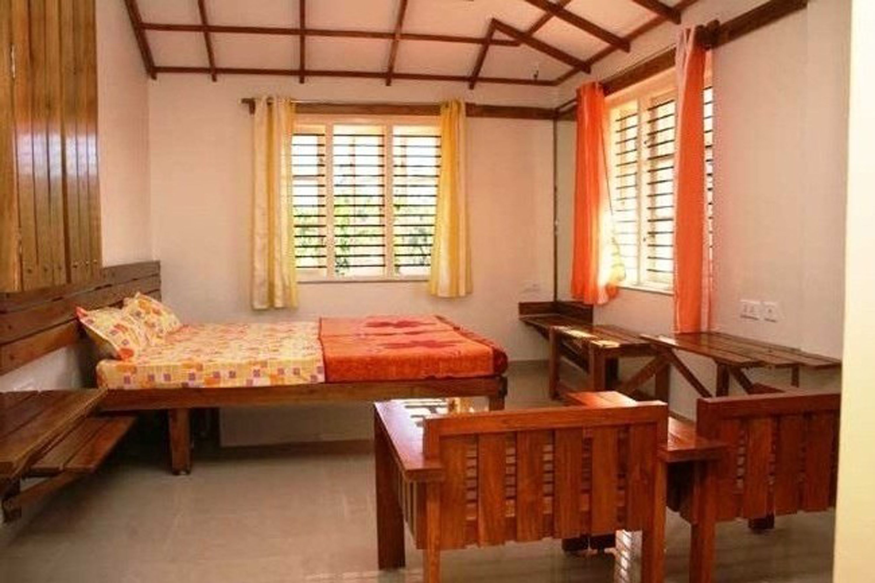 A room with a bed, wooden benches, and a window with curtains.