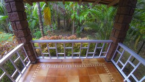 A covered outdoor area with a tiled floor and white railings, surrounded by lush greenery. - Matthuga (Siddapur)