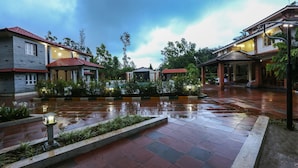 A courtyard with a wet tiled floor, surrounded by buildings with red roofs and a covered seating area. - Matthuga (Siddapur)