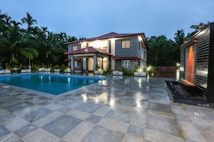 Una casa de dos pisos con piscina, rodeada de palmeras y un patio con baldosas.