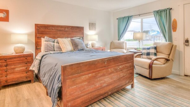 A bedroom with a wooden bed, a chair, a nightstand, and a window with curtains.