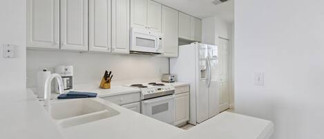 A modern kitchen with white cabinetry, a microwave, a refrigerator, a stove, and a sink.