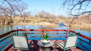 Une terrasse avec deux chaises et une table, donnant sur une rivière bordée d’arbres.