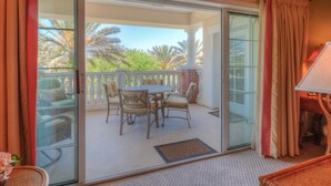 A balcony with a table and chairs, a view of palm trees, and a sliding glass door.