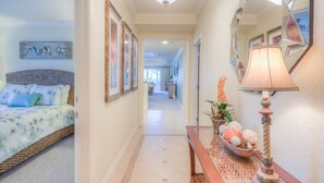 A hallway with a bed, a mirror, a lamp, and a decorative bowl on a console table.