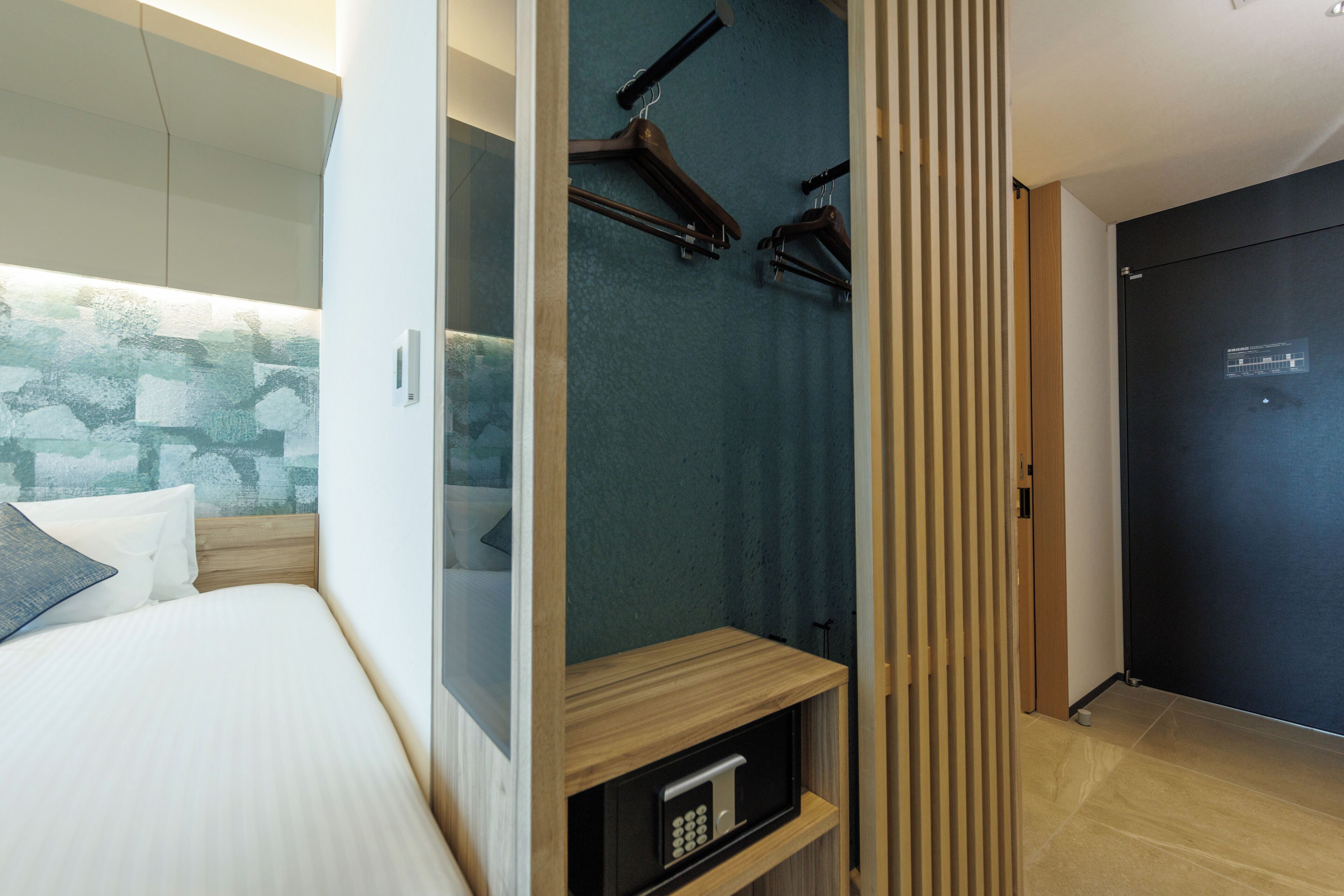 A modern hotel room with a bed, a built-in wardrobe, and a shower area.