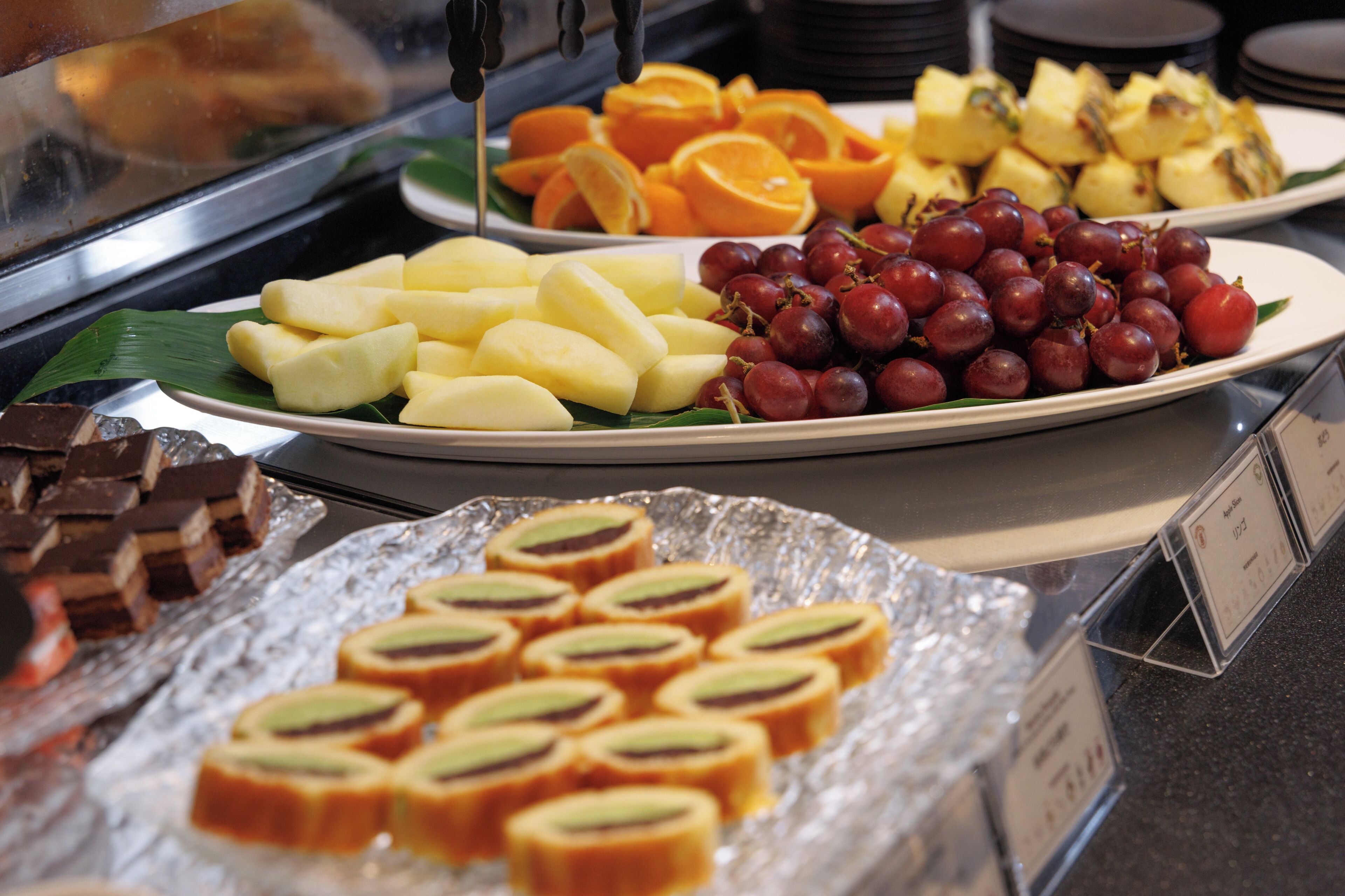 A buffet with various food items including sliced fruits, grapes, and pastries.