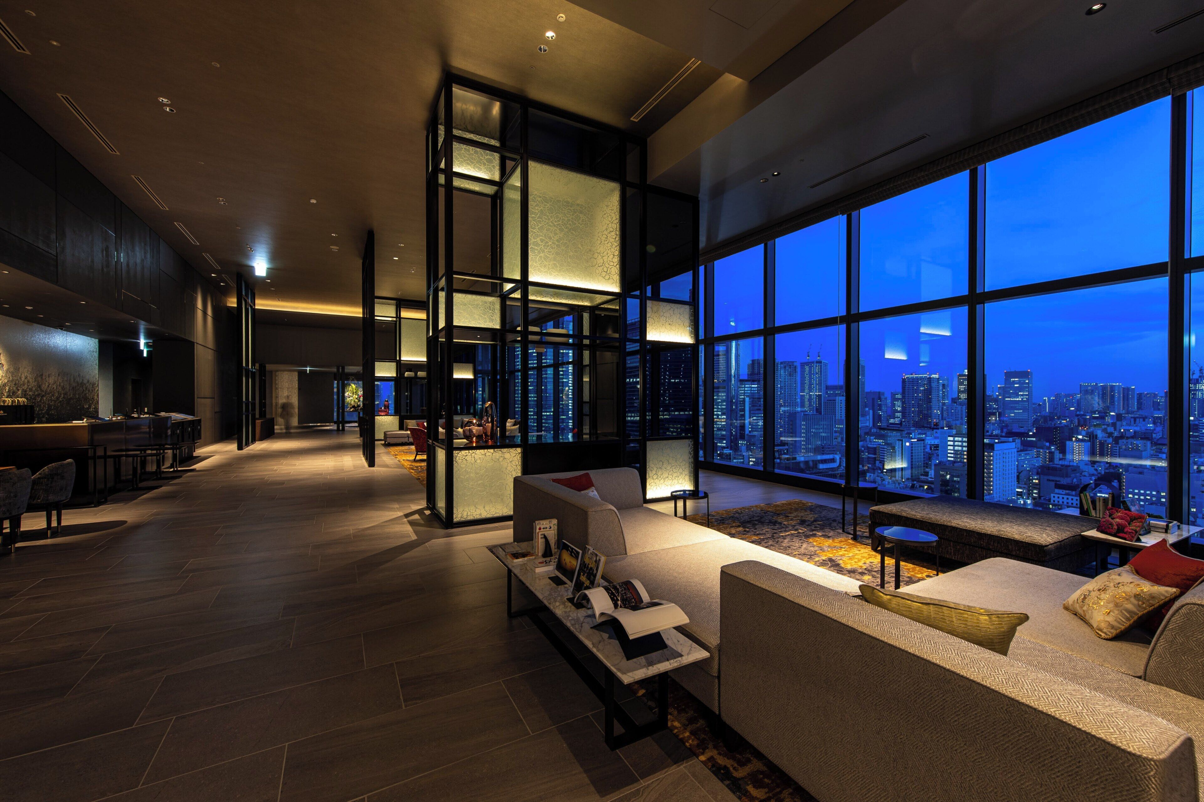 A spacious living area with a large window offering a city view, a seating area with a coffee table, and a reception desk.