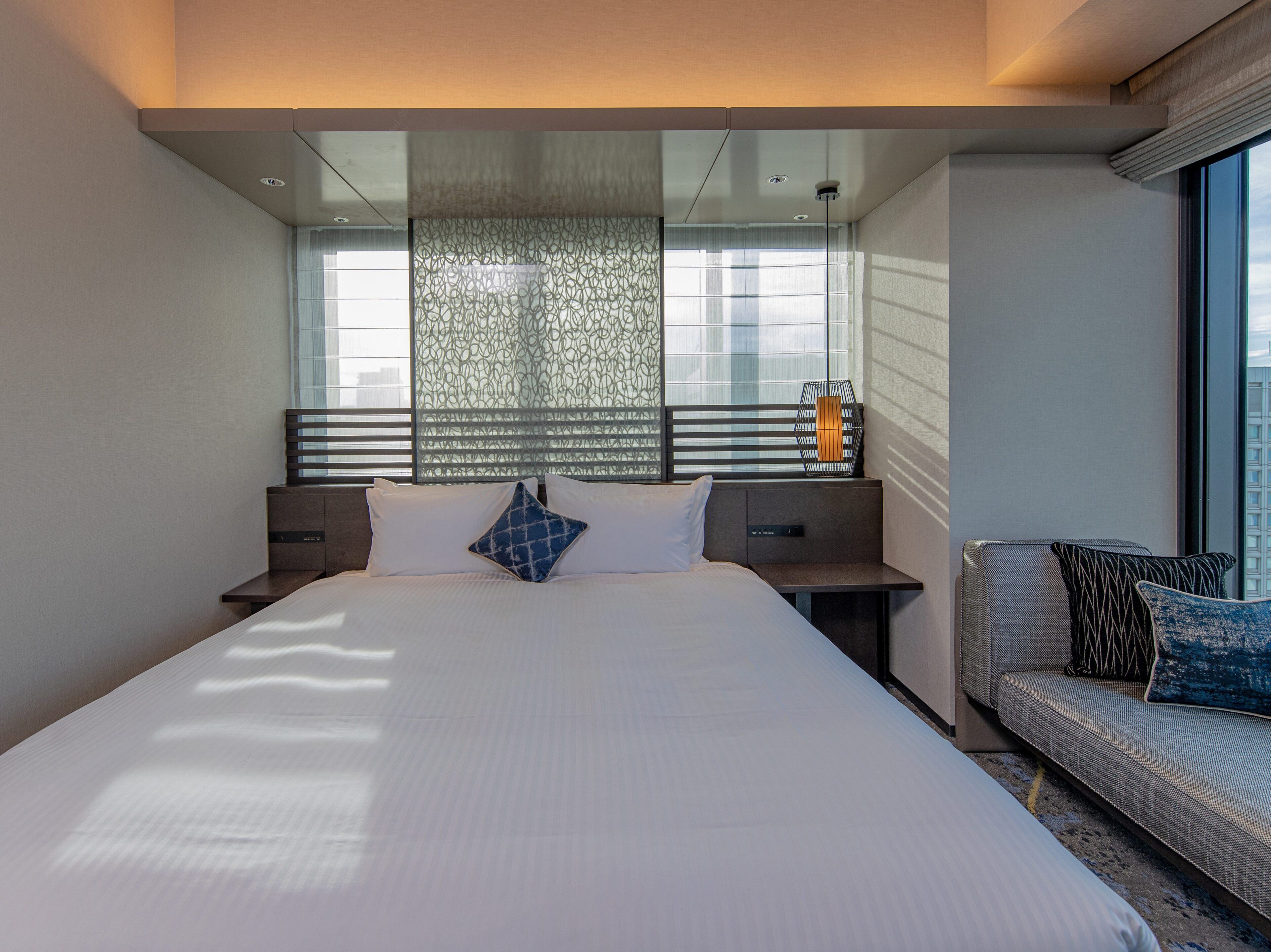 A modern hotel room with a large bed, a seating area, and a view of the city.