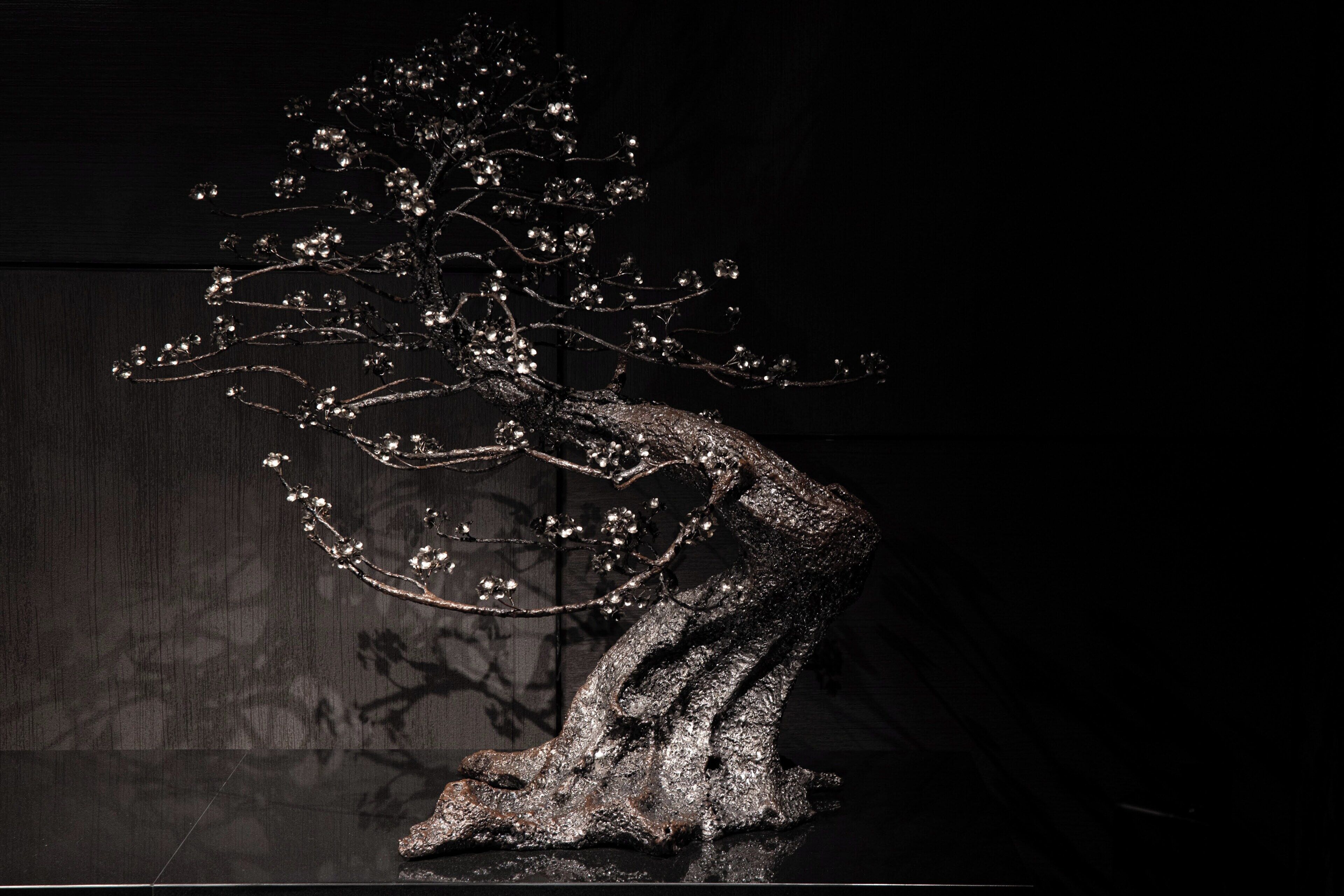 Una escultura de un árbol con tronco texturizado y ramas decoradas con detalles reflectantes.