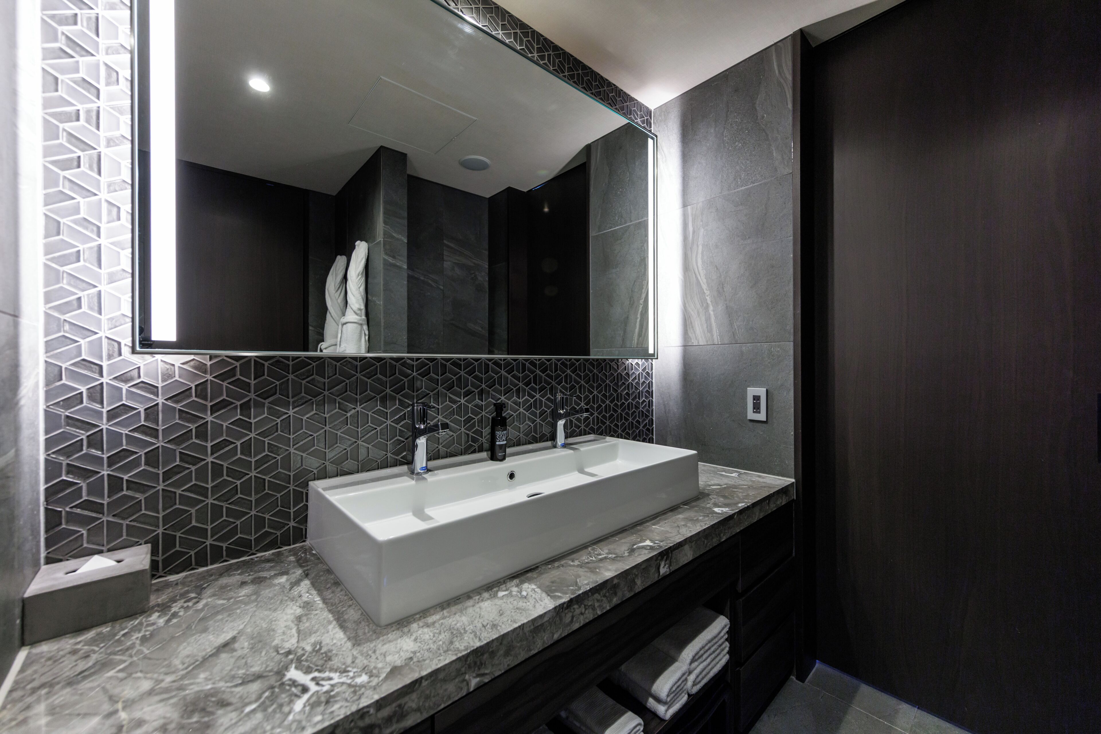 A modern bathroom with a rectangular sink, a large mirror, and a geometric patterned wall.