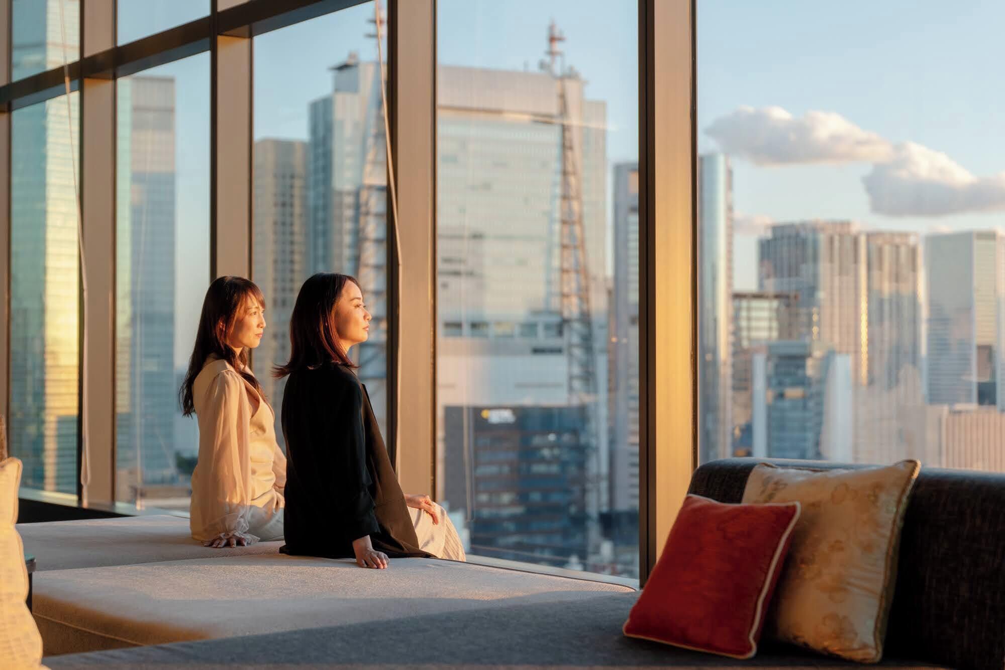 Deux personnes assises sur un balcon, avec vue sur le paysage urbain.