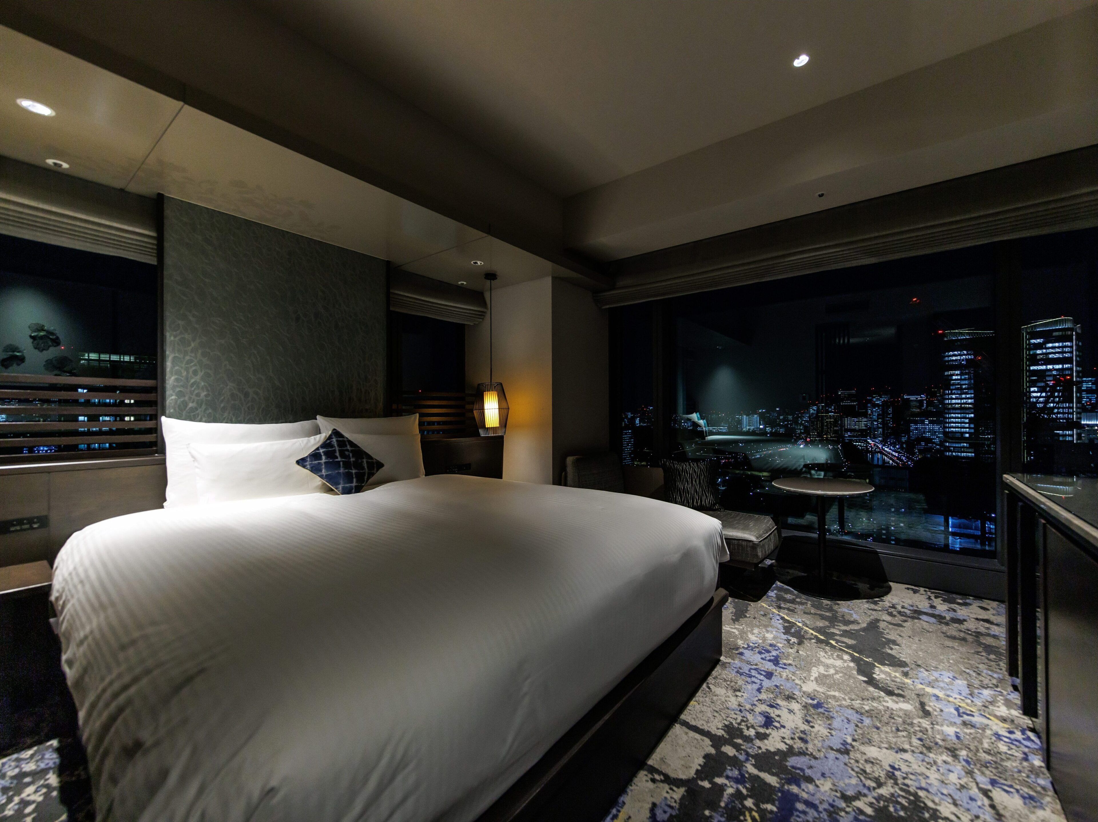 Ein Hotelzimmer mit einem großen Bett, Blick auf die Stadt, einem Schreibtisch und einem Stuhl.