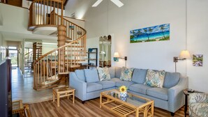 Un vaste espace de vie agrémenté d’un escalier en bois, d’un canapé bleu clair et d’un ventilateur de plafond.