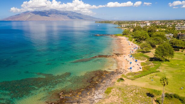 Une zone côtière avec une plage, des eaux cristallines et une montagne en arrière-plan.