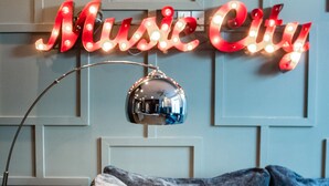 A neon sign reading "Music City" on a wall, a sofa with a cushion that says "Stay x Minty", and a decorative mirror. - 🏙️ Views 🌆 from Spectacular Rooftop | 🔥Fire Pit | Bach Groups!💃🏼🕺🏼 (Nashville)