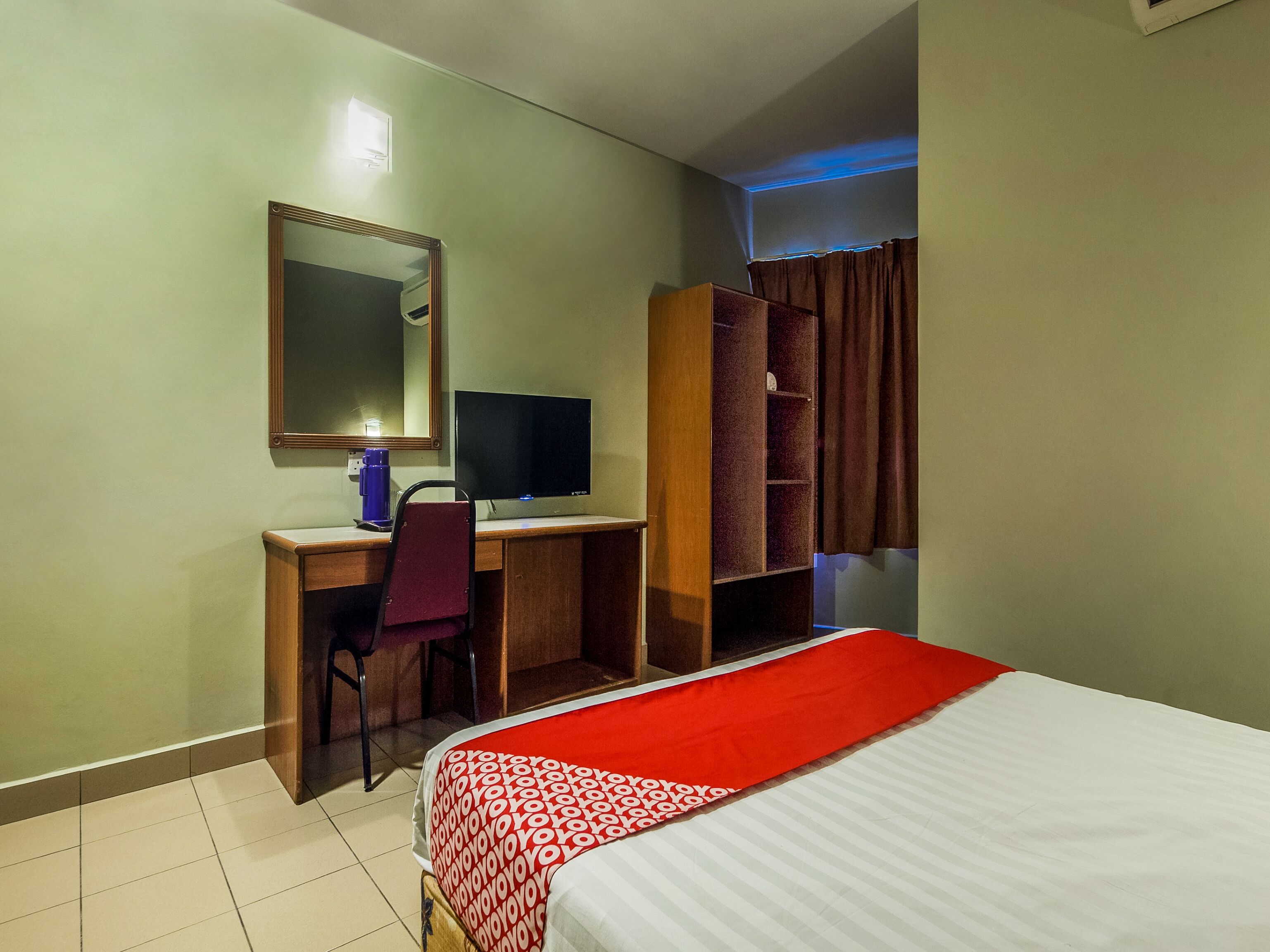 Una habitación de hotel con una cama, un escritorio con computadora, una silla, un armario y un espejo.