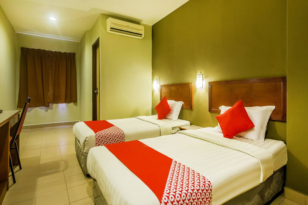 A hotel room with two beds, each with red and white bedding, a wooden headboard, and a wall-mounted air conditioner.
