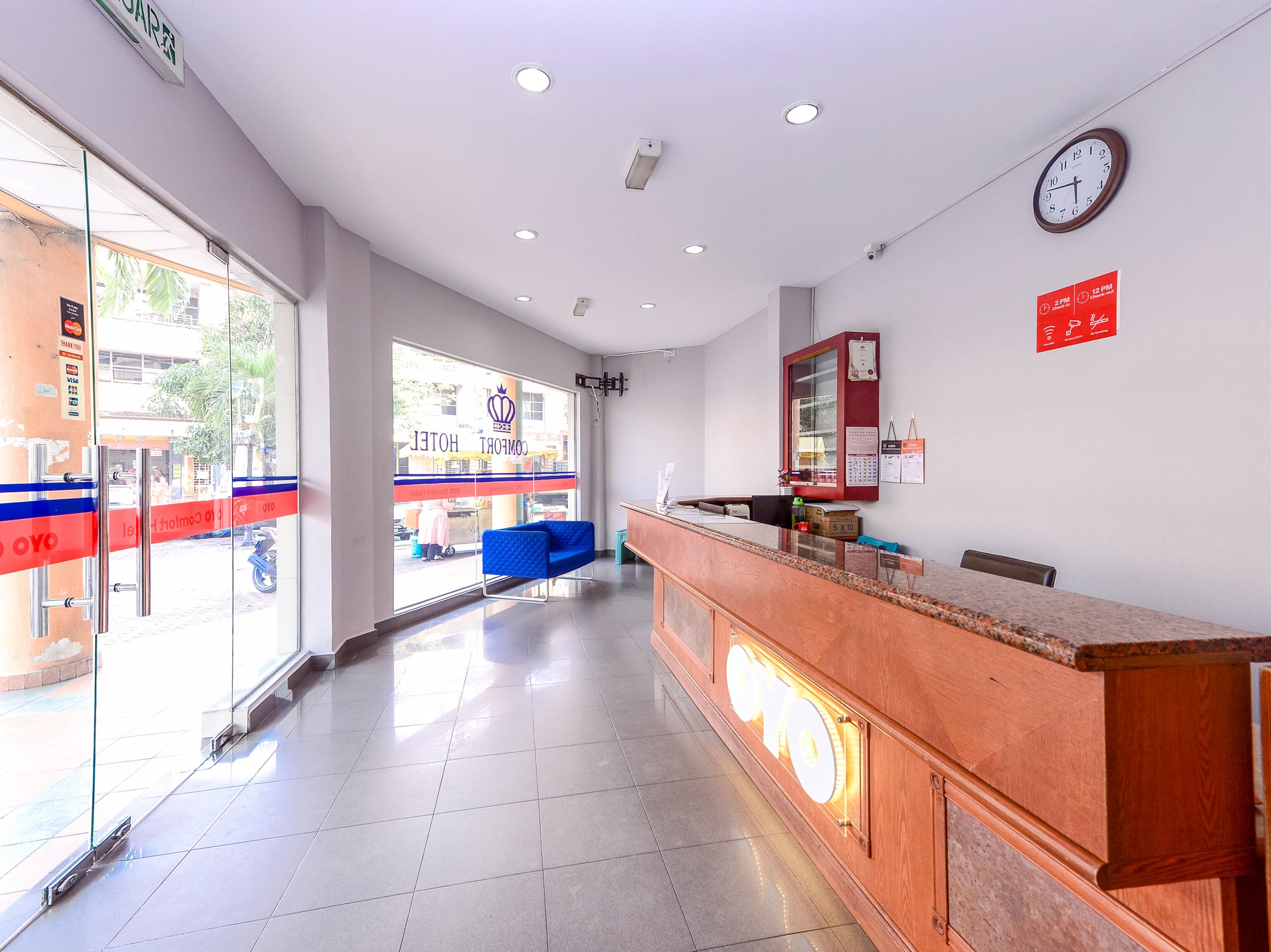 Zona de recepción de hotel con un mostrador de madera, un reloj y un letrero rojo que indica el horario de atención.