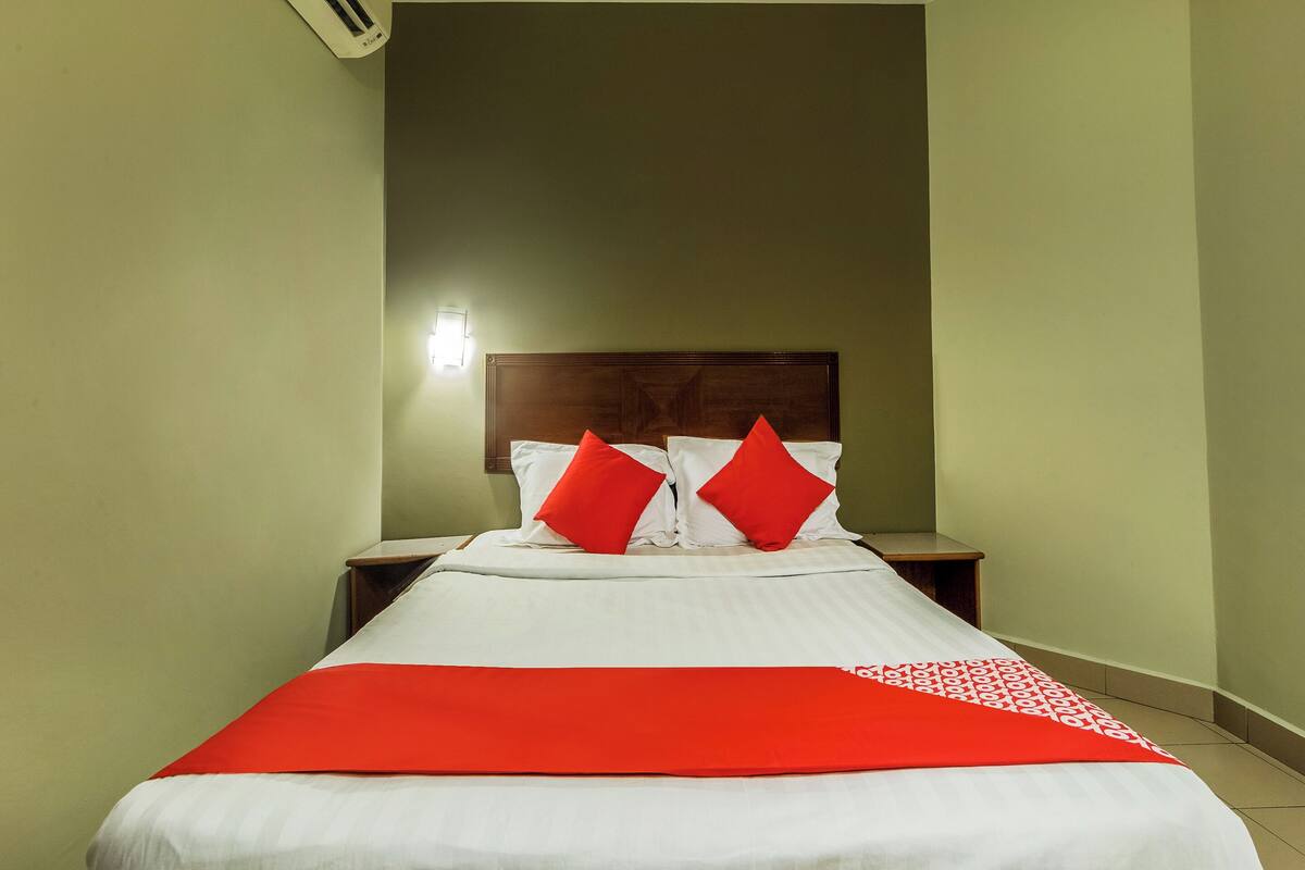 A neatly made bed with white bedding and red accents, a wooden headboard, and a small bedside table with a lamp.